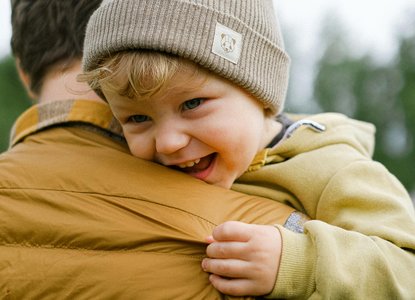 A toddler in a woolly hat carried by his dad