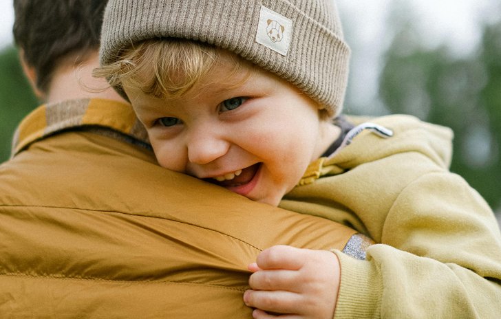 A toddler in a woolly hat carried by his dad